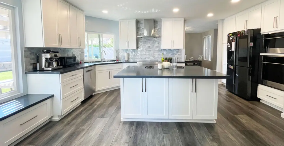 U shaped kitchen with an island. Whited painted shaker cabinets, charcoal soapstone quartz tops, full height marble subway tile backsplash, and stainless steel chimney style vent hood over range