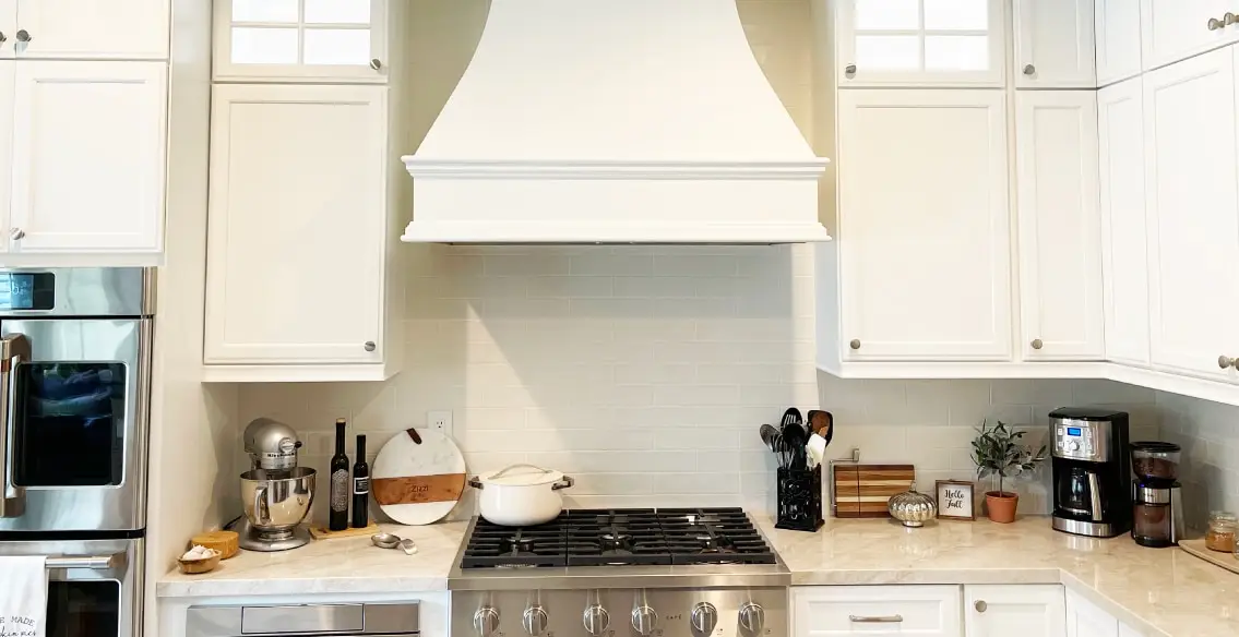 Close up shot of kitchen custom wood hood with white painted cabinets. Taj mahal quartzite, and full height white subway tile backsplash