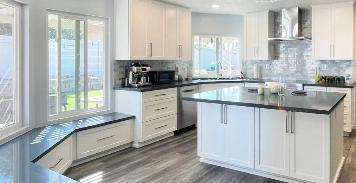 White painted shaker kitchen with charcoal soapstone quartz tops, stainless steel chimney style hood, and full height marble subway tile backsplash.