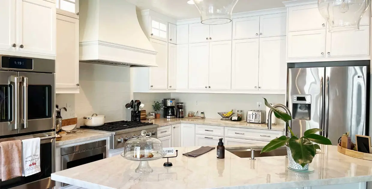 L shaped kitchen with an island. White painted modified shaker cabinets, decorative wood hood, full height white tile backsplash, and Taj Mahal quartzite countertops