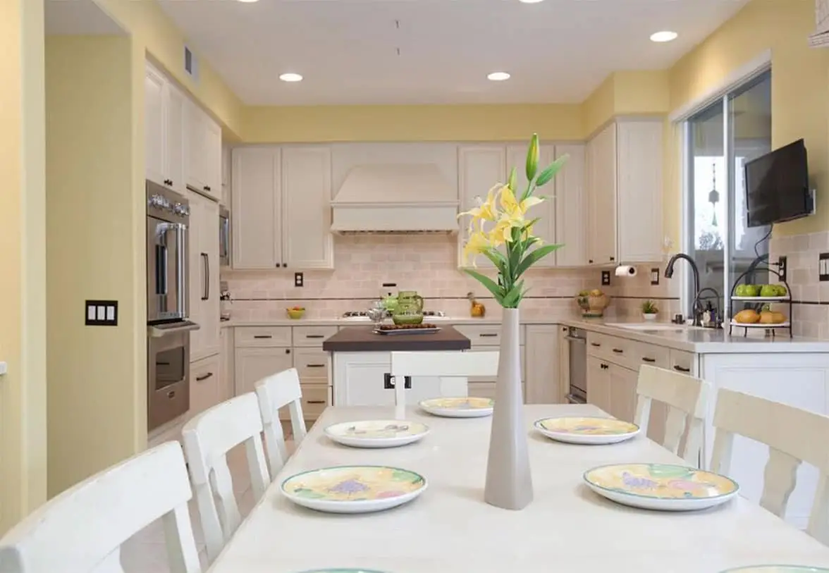 U shape kitchen with white painted cabinets and decorative wood hood, full height tile backsplash and dining table in the foreground.