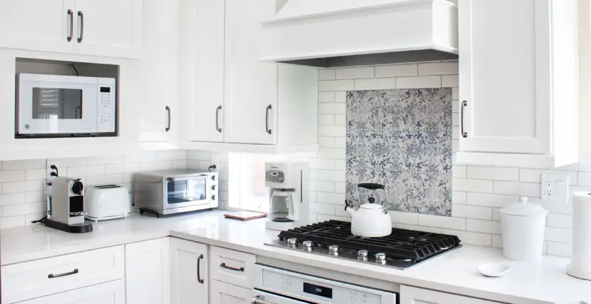Kitchen with white painted cabinets, custom wood hood, white subway full height tile splash, and blue decorative tile above range.