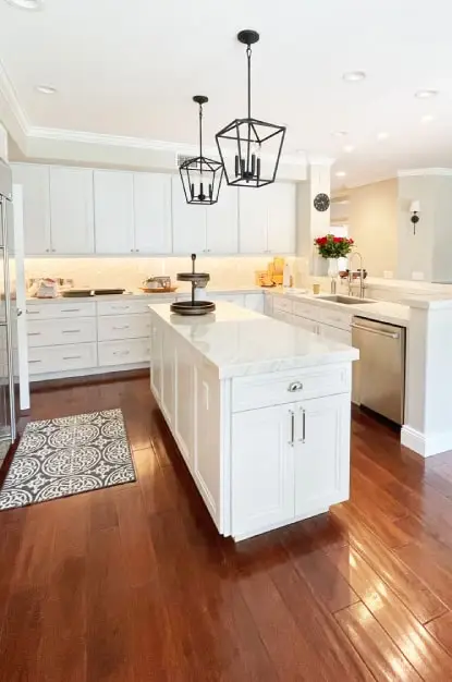 U shaped kitchen with island. White painted modified shaker cabinets with Perla Venata quartzite countertop and full height splashes. Black pendant lights hanging over island and cherry wood floors.