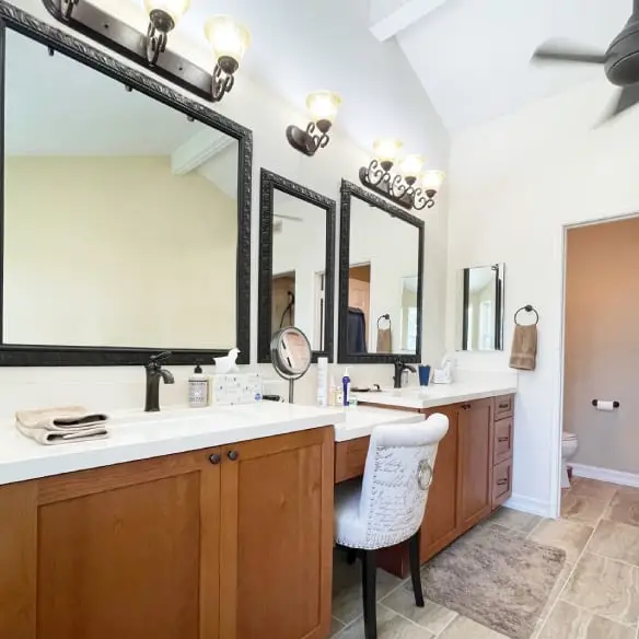 Double sink vanity area with makeup drawer and chair in center. Warm tone wood cabinets and oil rubbed bronze fixtures.