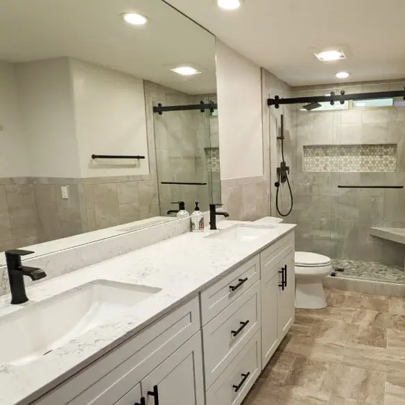 Double sink vanity with white cabinets, quartz top, and black fixtures. Tiled shower with custom barn style sliding shower door and tile floor.