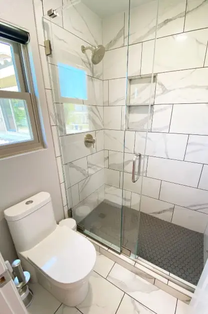 Custom tiled shower with 12x24 marble look tile on the walls and grey hexagon tile on the shower pan. Custom frameless sliding shower door.