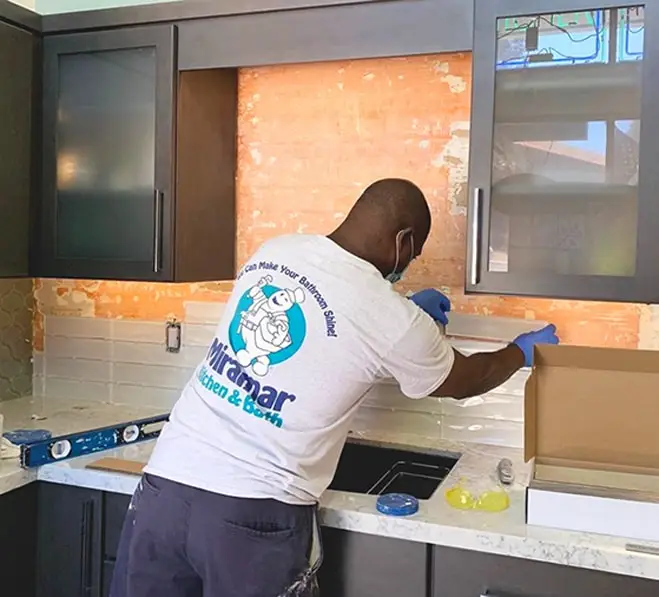 An installer from Miramar Kitchen & Bath working on a tile backsplash in a kitchen display.
